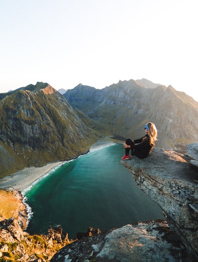 女人坐在悬崖俯瞰山脉附近的水域在白天
